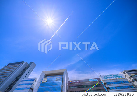 日本橫濱的街景。新橫濱車站前的建築物、飛機的軌跡與陽光。邁向新時代 = 7月19日 128625939