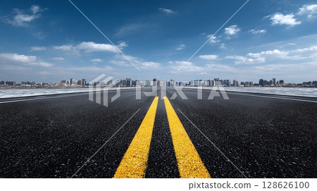 Road to the City: A long highway stretches towards a skyline under a bright blue sky, promising journeys and adventures towards the urban landscape ahead. 128626100