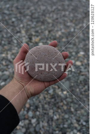 round stone in the hand of a man on the background of the stone beach 128628127