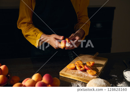 Hands Preparing Fresh Apricots on a Wooden Cutting Board in a Kitchen with Warm Lighting 128628160