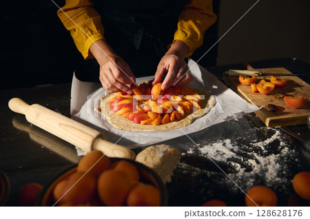 Woman Arranging Fresh Apricot Slices on Rustic Tart Dough for Homemade Dessert Woman Arranging Fresh Apricot Slices on Rustic Tart Dough for Homemade Dessert 128628176