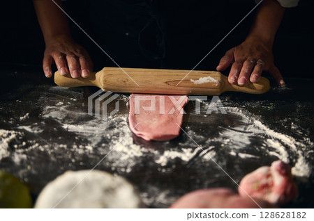 Chef Rolling Pink Pasta Dough in Kitchen Showing Culinary Craftsmanship Chef Rolling Pink Pasta Dough in Kitchen Showing Culinary Craftsmanship 128628182