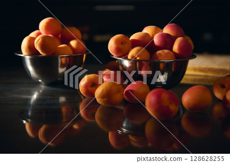 Fresh Apricots in Metal Bowls on a Reflective Surface with Warm Lighting 128628255