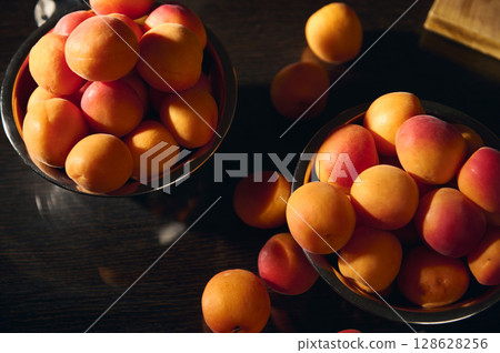 Fresh Ripe Apricots in Metal Bowls on a Wooden Tabletop Surface 128628256