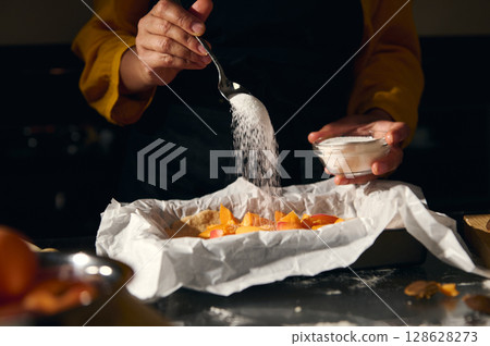 Chef Sprinkling Sugar on Fresh Ingredients for Baking in a Cozy Kitchen Setup 128628273