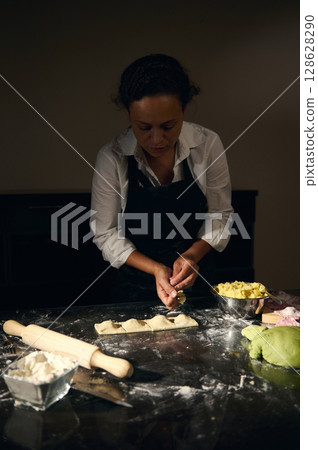 Woman Chef Preparing Ravioli Pasta with Italian Flag Colored Dough in a Traditional Kitchen Setting Woman Chef Preparing Ravioli Pasta with Italian Flag Colored Dough in a Traditional Kitchen Setting 128628290