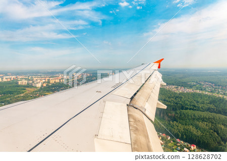 View of airplane wing, blue skies and green land during landing. Airplane window view. 128628702