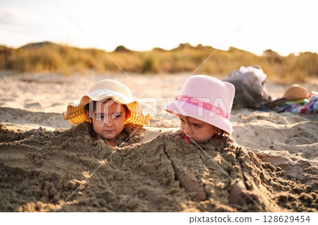 Sisters enjoy a sunny day at the beach while building sandcastles 128629454