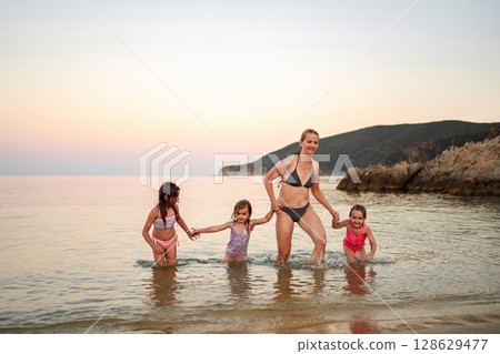 Joyful family splashes in shallow water at sunset beach retreat 128629477