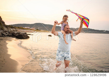 Family enjoys a colorful day flying a kite by the serene beach waters 128629496