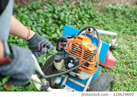 Gardener carefully mowing the green lawn with a modern lawn mower on a sunny day outdoors. 128629600