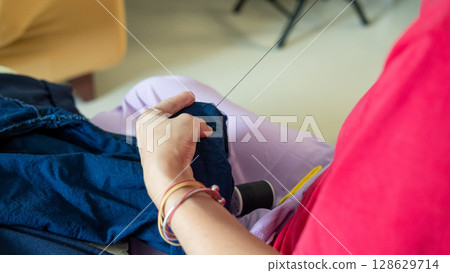 A mother hands carefully sewing trouser legs to mend clothes for her child at home 128629714
