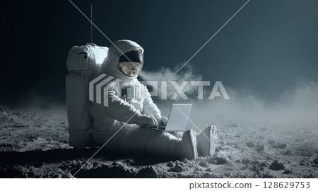 Astronaut works on a laptop while sitting on a lunar surface. A futuristic blend of technology and space exploration in a muted color palette. 128629753