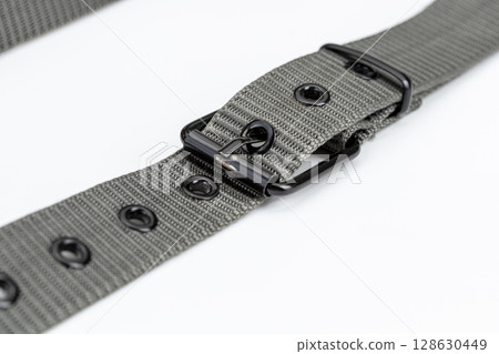 Close up of gray nylon belt with metal buckle, showcasing its durable design and multiple eyelets. belt is laid out on white background, highlighting its texture and functionality 128630449