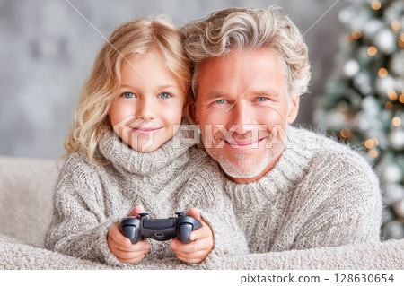 Grandfather and granddaughter enjoying video game together in cozy living room during holidays 128630654