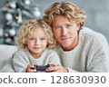 Father and child enjoying video game together in cozy winter setting with festive decorations 128630930