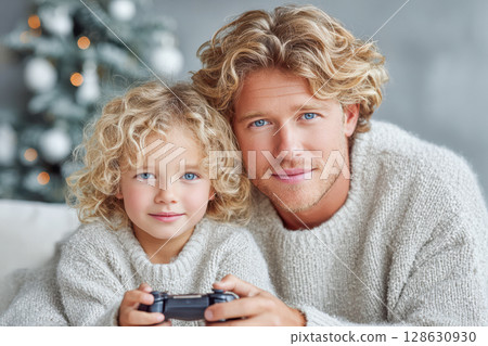 Father and child enjoying video game together in cozy winter setting with festive decorations Father and child enjoying video game together in cozy winter setting with festive decorations 128630930