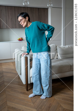 Healthcare issues with back ache. Mature woman in pain clutching on sofa, back hernia attack 128631393