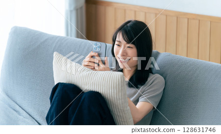 微笑的女人坐在沙發上使用智慧型手機 微笑的女人坐在沙發上使用智慧型手機 128631746