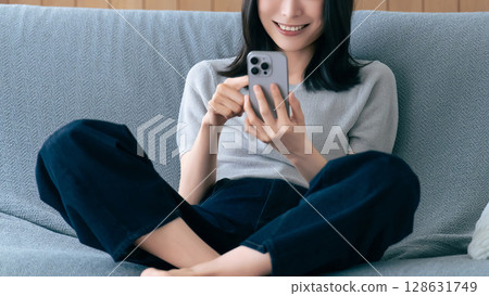 微笑的女人坐在沙發上使用智慧型手機 微笑的女人坐在沙發上使用智慧型手機 128631749