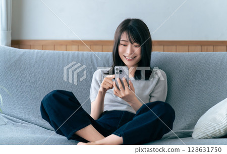 微笑的女人坐在沙發上使用智慧型手機 微笑的女人坐在沙發上使用智慧型手機 128631750