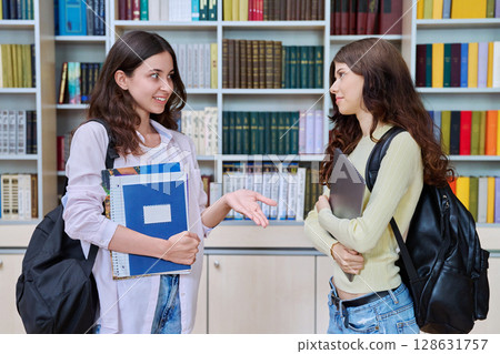Two teenage students classmates chatting standing in classroom library Two teenage students classmates chatting standing in classroom library 128631757