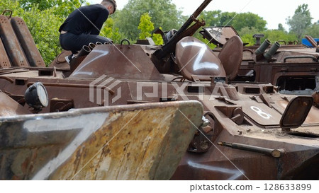 Young man looking at destroyed military equipment of the russian army. Exhibition of rusty and burned-out armored vehicles on ukrainian territory. War between Ukraine and russia. Slow motion 128633899