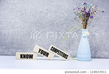 KNOW YOUR COMPETITORS text on wooden blocks on a gray background next to a flower KNOW YOUR COMPETITORS text on wooden blocks on a gray background next to a flower 128633911