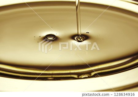 Pouring oil in golden tones. The texture of a cosmetic or other oil product. 128634916