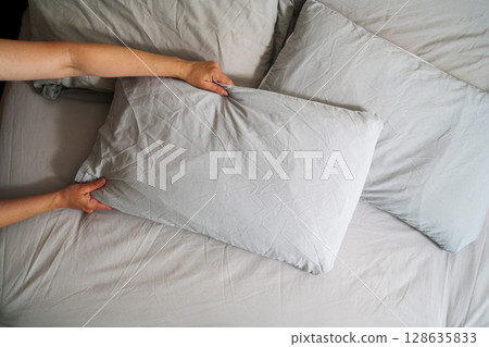 Female hands holding a pillow with fresh clean pillowcases, grey cotton bed sheets Female hands holding a pillow with fresh clean pillowcases, grey cotton bed sheets 128635833
