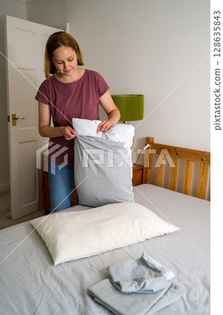 Woman changing pillow case with fresh clean grey cotton bed sheets Woman changing pillow case with fresh clean grey cotton bed sheets 128635843