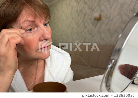 A charming senior woman is at her house, beautifying herself for the morning. 128636055