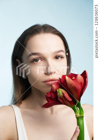 Young woman holds red flower against blue background with soft lighting 128636073