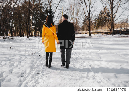 Couple walks hand in hand through snowy park in winter 128636078