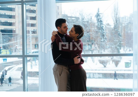 Couple embraces warmly inside bright, modern space during winter season Couple embraces warmly inside bright, modern space during winter season 128636097