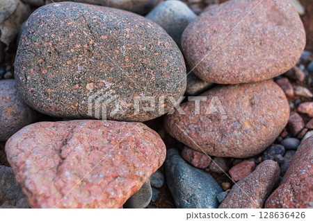 Large river red polished rounded stones pebbles with inclusions of white, black grains, lying on the bottom of a dry river close-up. Natural ceramic materials in environment, background 128636426