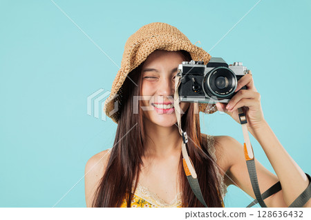 Happy asian woman travel close up, smiling tourist is taking photo with a camera wearing a hat on holiday vacation, she seems happy to travel and take photos, headshots isolated studio blue background Happy asian woman travel close up, smiling tourist is taking photo with a camera wearing a hat on holiday vacation, she seems happy to travel and take photos, headshots isolated studio blue background 128636432