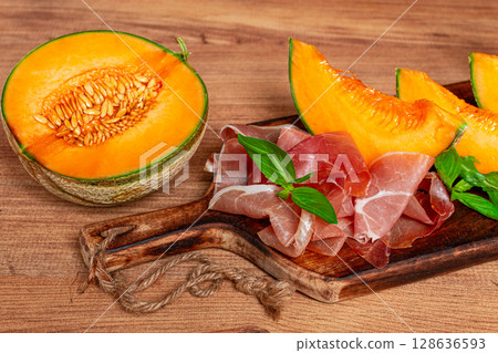 cantaloupe melon, with prosciutto, and fresh basil, on a wooden serving board, rustic style, 128636593