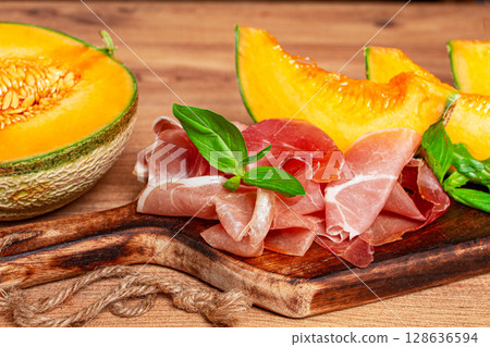 cantaloupe melon, with prosciutto, and fresh basil, on a wooden serving board, rustic style, cantaloupe melon, with prosciutto, and fresh basil, on a wooden serving board, rustic style, 128636594