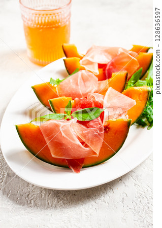 Cantaloupe melon with prosciutto and fresh basil, on a white plate, natural light, Cantaloupe melon with prosciutto and fresh basil, on a white plate, natural light, 128636597