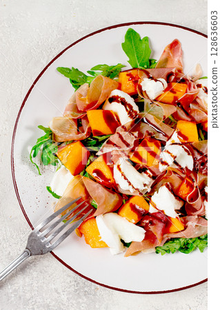 salad with slices of ripe melon, prosciutto, mozzarella and fresh arugula, decorated with balsamic glaze. salad with slices of ripe melon, prosciutto, mozzarella and fresh arugula, decorated with balsamic glaze. 128636603
