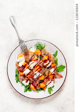 salad with slices of ripe melon, prosciutto, mozzarella and fresh arugula, decorated with balsamic glaze. 128636604