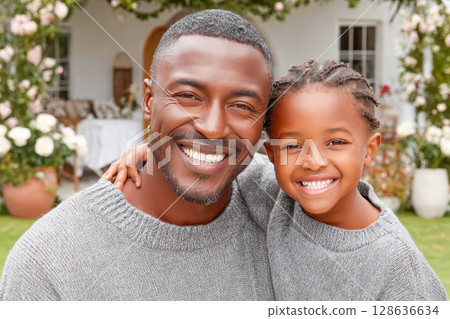 Smiling father and daughter wearing matching sweaters in a garden with blooming flowers 128636634