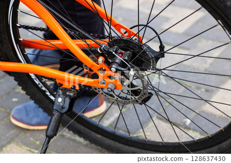 A person stands next to an orange bicycle with a disc brake 128637430