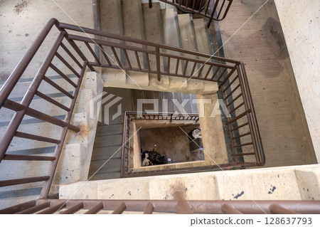 Looking down the center of a twisting stairwell in a parking ramp with trash and dirt Looking down the center of a twisting stairwell in a parking ramp with trash and dirt 128637793