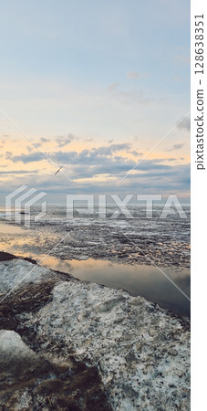 Peaceful scene of ice floes drifting in calm ocean waters with stunning sunset sky. Reflective water surface captures colorful clouds, evoking serenity and tranquility. Vertical photo Peaceful scene of ice floes drifting in calm ocean waters with stunning sunset sky. Reflective water surface captures colorful clouds, evoking serenity and tranquility. Vertical photo 128638351