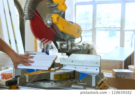 Trim worker operates miter saw, cutting molding with precision in home renovation interior Trim worker operates miter saw, cutting molding with precision in home renovation interior 128639382
