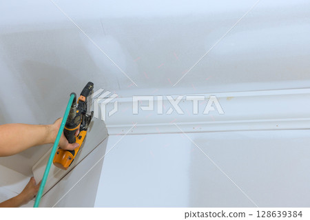 Carpenter is installing crown molding in contemporary room using power tool for pneumatic nail gun Carpenter is installing crown molding in contemporary room using power tool for pneumatic nail gun 128639384