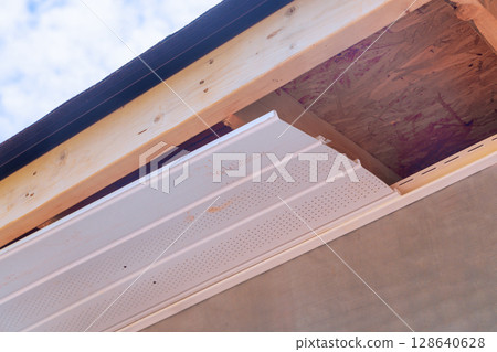 Workers are installing siding panels construction plastic soffit material in eaves on house Workers are installing siding panels construction plastic soffit material in eaves on house 128640628