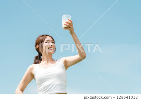 Woman drinking protein/EAA drink during exercise (blue sky) 128641018